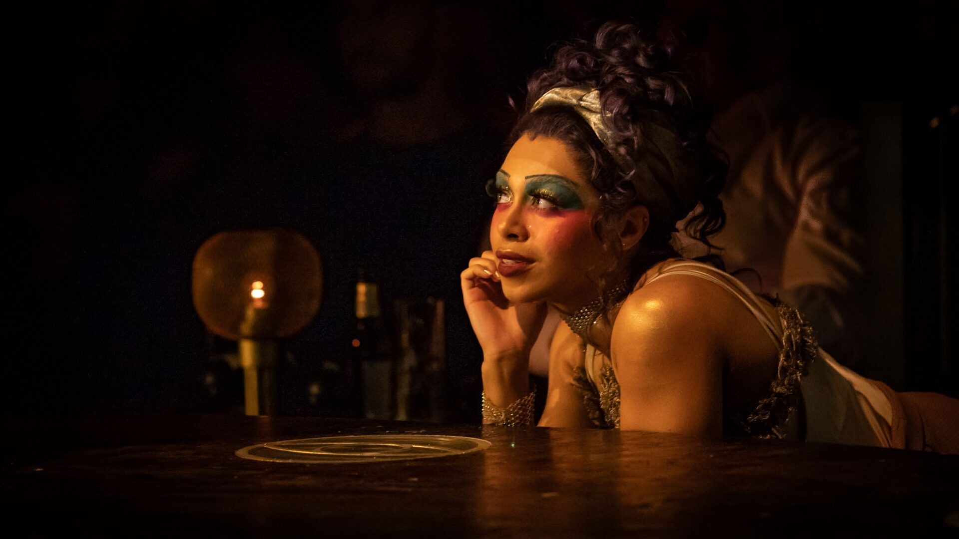 Production photo of actress looking into the distance with her hand on her chin