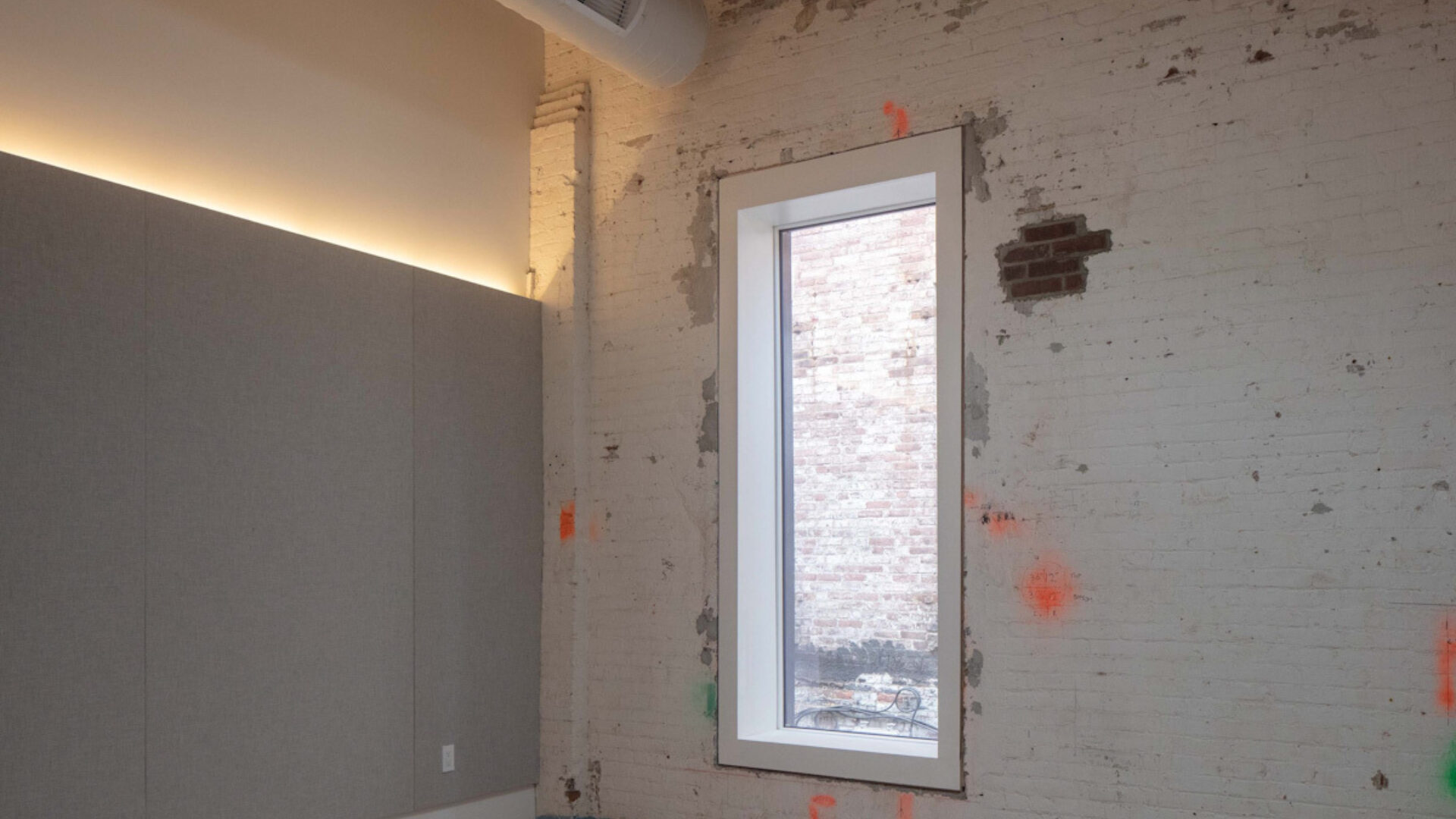 Interior of rehearsal room at Mercury store, with grey acoustic panel ont eh left wall and one window on the right with a rustic finish